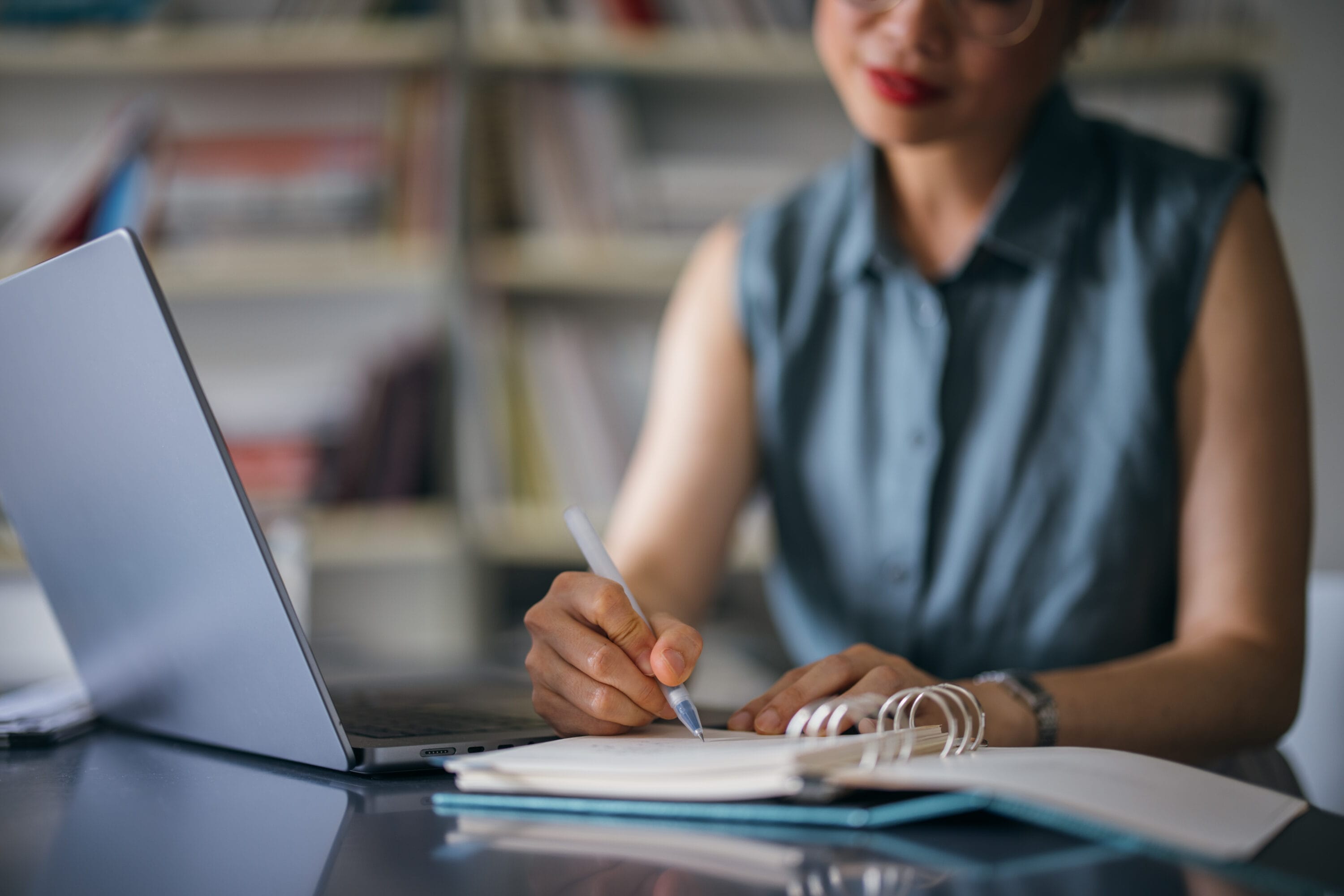 A closeup of a woman at a her table with a notebook at her side and a laptop in front of her
