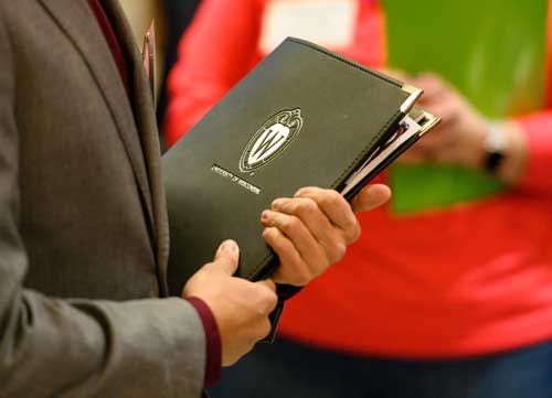 Close up of a pair of hands holding a notebook with the UW-Madison crest on the cover