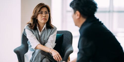 A woman and a man sitting down together, chatting,